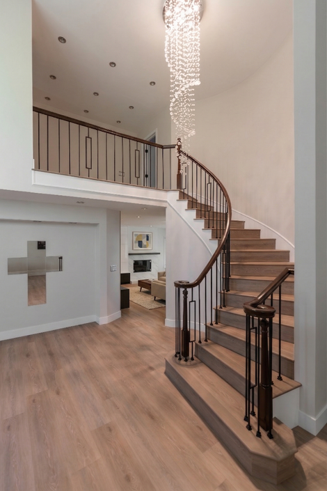 Grand curved staircase with light wood treads, dark wood railings, and a cascading crystal chandelier in a modern open-concept home. Serving Los Angeles County, Orange County, and San Bernardino County.