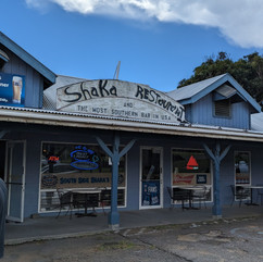 outside of restaurant with the sign "Shaka Restaurant" in large letters, and "The most southern bar in the USA" in small letters underneath. Restaurant has blue siding and looks worn