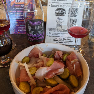 photo of a bowl of onions, prosciutto, and pickles. a few glasses of beer are visible, containing a dark red beer.