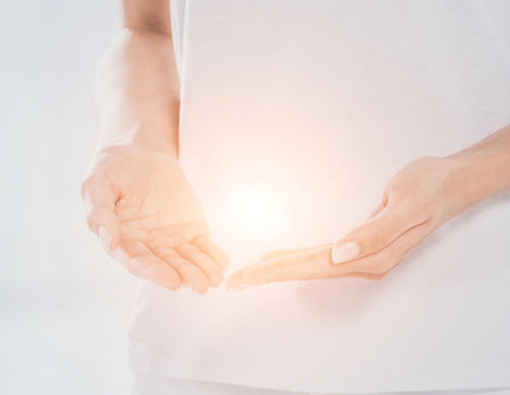 mid section of reiki healer with light energy in hands standing near white massage table _
