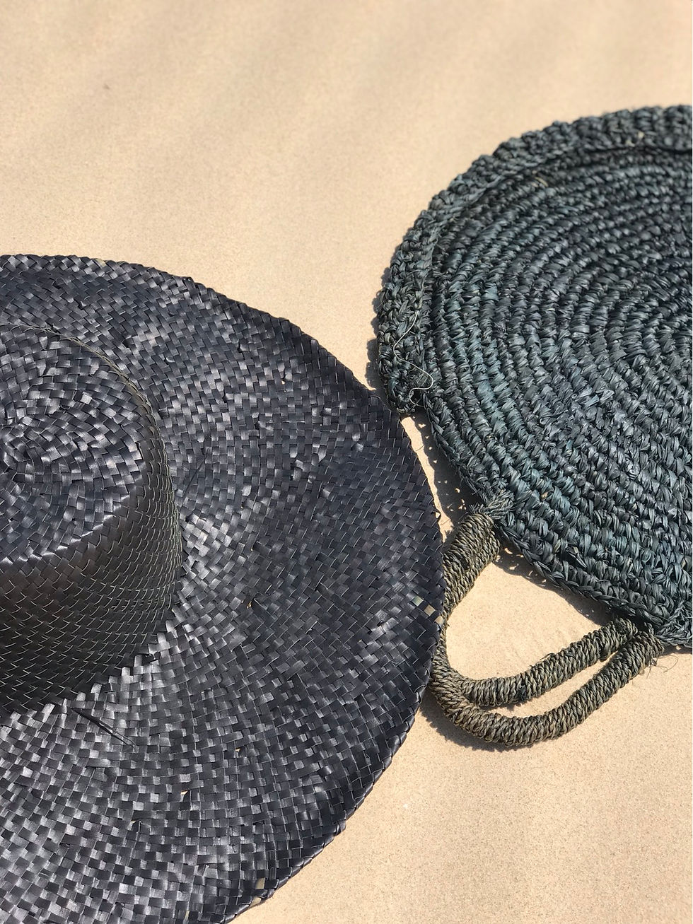 תמונה ממוזערת: תיק קש וכובע קש בצבע שחור מונחים על החול