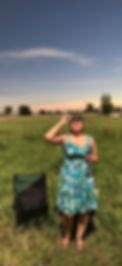 Woman standing in a field holding eclipse glasses