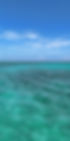 Various shades of blue and turquoise water seen from a water taxi on a clear sunny day in Belize, with a few wisps of clouds in the sky