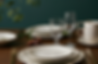 Fine dining table setting with stacked white plates, silverware, water glasses and wine glass against a green background.