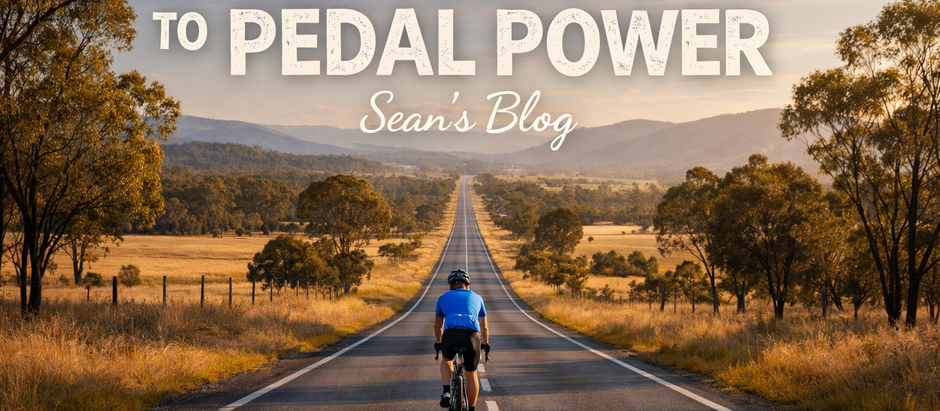 A cyclist with a light blue shirt and dark pants riding down the centre of an open Australian highway with farmland, natural bush, eucalyptus trees to the sides and hills off in the distance