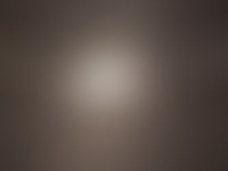 A close-up image shows a silver nameplate necklace resting on a dark, textured surface. The chain stretches from both sides toward the center, where a shiny pendant spells “RIVER” in bold capital letters. Beneath the name, decorative symmetrical swirls extend outward, with a small heart shape in the middle. The polished metal reflects light, making the letters and heart gleam against the dark background.