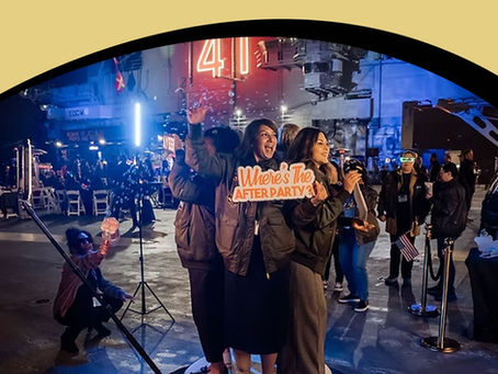 Two women posing on a rotating 360 video booth platform at an outdoor event, holding a sign that says "Where's The AFTER PARTY?".