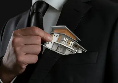 Businessman placing a small model house into his suit pocket.