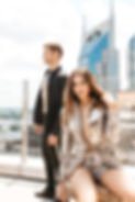 A woman in a silver sequined outfit poses seated while a man in a black suit stands behind her on a rooftop with Nashville skyscrapers in the background. Captured by Weatherly Photography, the image epitomizes chic city lifestyle.