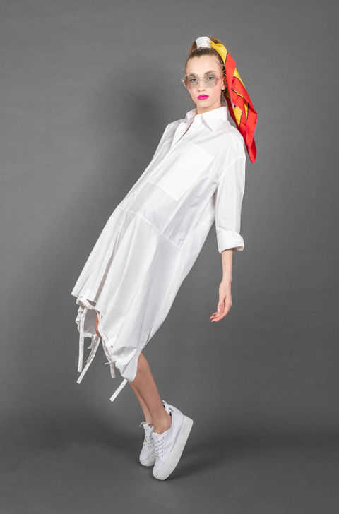 A person wearing a white dress, white sneakers, sunglasses, and a colorful scarf on their head poses against a gray background, embodying the essence of weatherly photography for branding purposes.