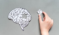 Female hand trying to connect a missing jigsaw puzzle of human brain on gray background. C