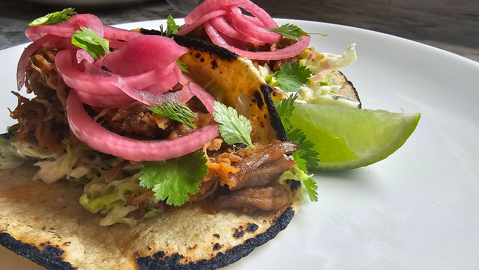 Savor the taste of smoky pulled pork tacos topped with tangy pickled onions, fresh cilantro, and a wedge of lime for a zesty finish.