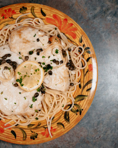 A plate of linguini chicken picatta, garnished with lemon and capers