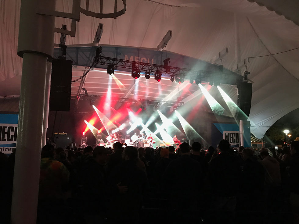 A packed crowd stands in silhouette beneath a dramatic canopy of red and white stage lights at MECU Pavilion in Baltimore, as Umphrey's McGee performs on stage in the distance.