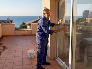 Un laveur de vitres s’affaire à nettoyer la baie vitrée d’une grande villa.