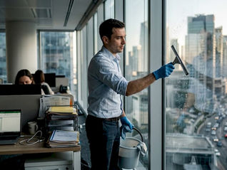 Un agent d’entretien nettoie les vitres dans un bureau en ville.