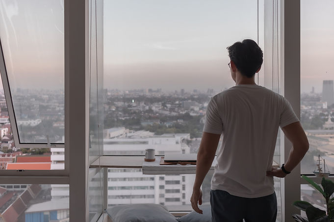 man-stand-window-apartment-looking-out-city-view.jpg
