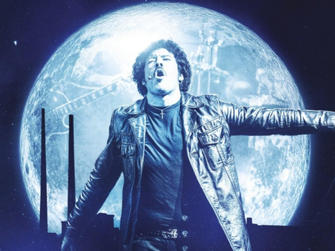 Man in black leather jacket sings passionately with arms outstretched against a bright moonlit background, exuding dramatic emotion.