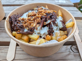 Beef brisket on top of French fries in a disposable bowl