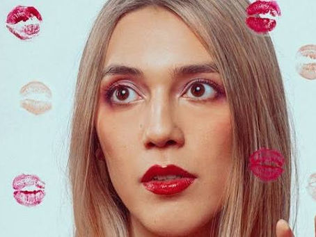 Close-up of a blonde woman with red lipstick against a pale blue wall, surrounded by lipstick kiss prints, looking surprised.
