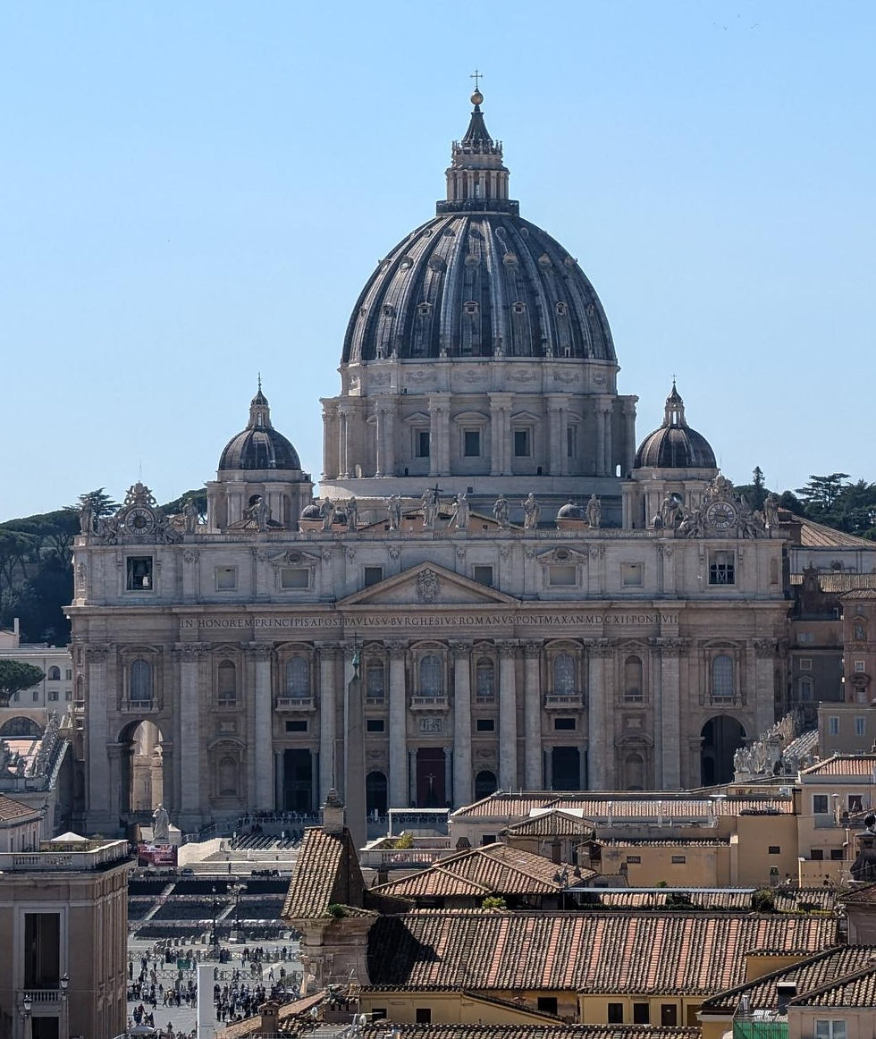 St. Peter's Basilica with its iconic dome looms over terracotta rooftops in Vatican City, set against a clear blue sky.