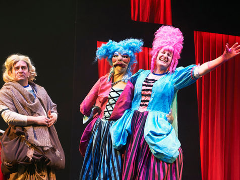 A man dresses in rags as Cinderella, with a second man attached to a full sized ventriloquist's dummy acting as the other ugly sister