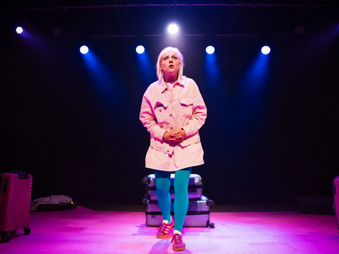 Woman standing on a stage with suitcases piled behind her