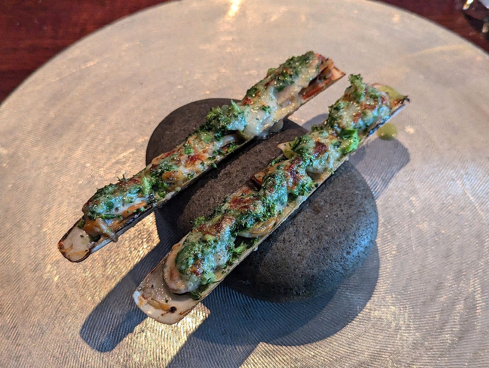 Gratin of razor clams and mussels served in razor clam shells balanced on a pebble