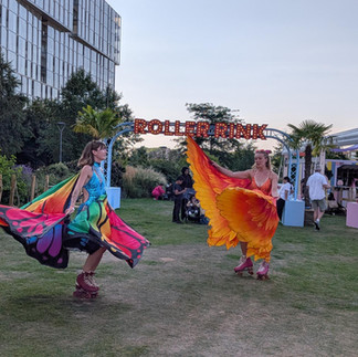 Two women dressed in bright coloured clothing show off their roller skating skills on the grass