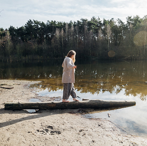 Eine Frau balanciert auf einem Baumstamm, der liegend in den See ragt.