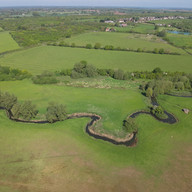An overhead drone shot of a winding river surrounded by trees and lush green banks