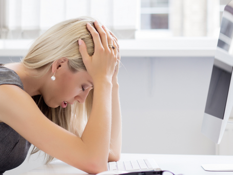 essoa exausta sentada com as mãos no rosto, representando os sintomas do burnout, como cansaço extremo e sobrecarga emocional no ambiente de trabalho.