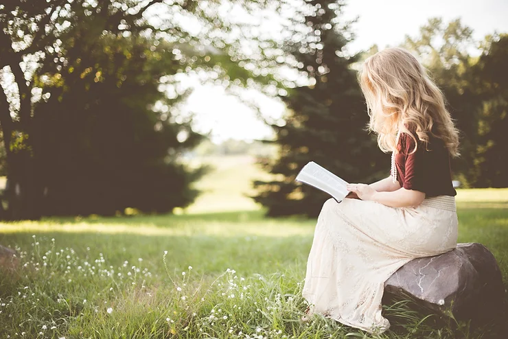 A woman sitting outdoors reading the bible