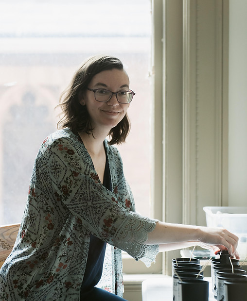 Brunette women smiling next to a window while working on candles
