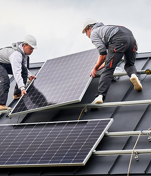 Installers installing solar panel system on roof of house. Men workers in helmets carrying