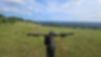 Bicycle handlebars in foreground, overlooking a vast green landscape. Blue sky with clouds. People sit in the distance enjoying the view.