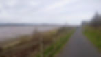 Pathway with a wooden fence beside a estuary with the tide out under a cloudy sky. A person walks in the distance. Peaceful and expansive mood.