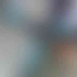 Person holding a bike with blue handlebars, wearing blue gloves and grey jacket. Bike has a device mount. Background is a concrete wall.