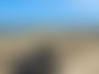 Bike leans against a concrete wall by a pebble beach. Sea and wind turbines in the background under a clear blue sky.