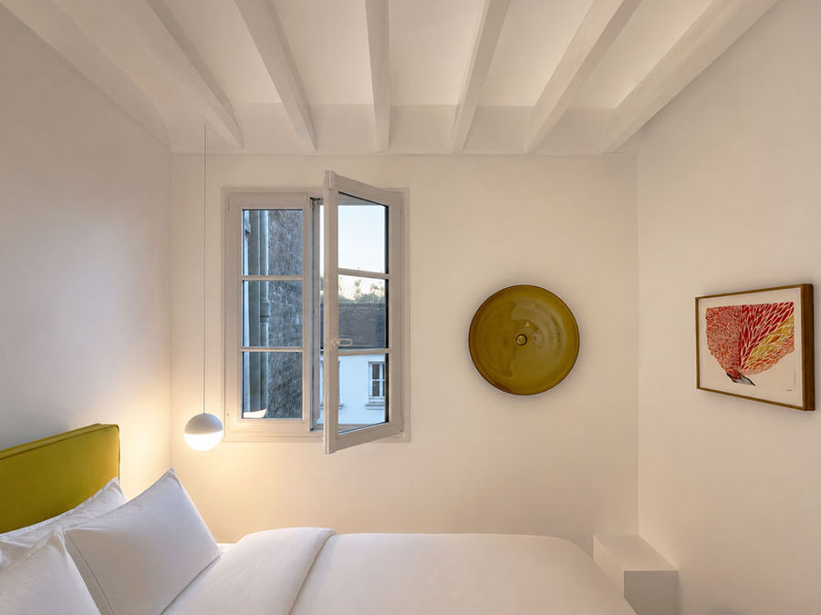 Du Bac Residence in Paris by Japanese architect kodai and associates, a gallery-like white bedroom for a contemporary art collector with painted timber rafters, soft ceiling light, curated art and quiet architectural textures.