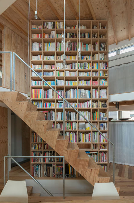 Tall bookshelf wall and timber staircase inside Kyodo House, a contemporary Japanese residence in Tokyo.