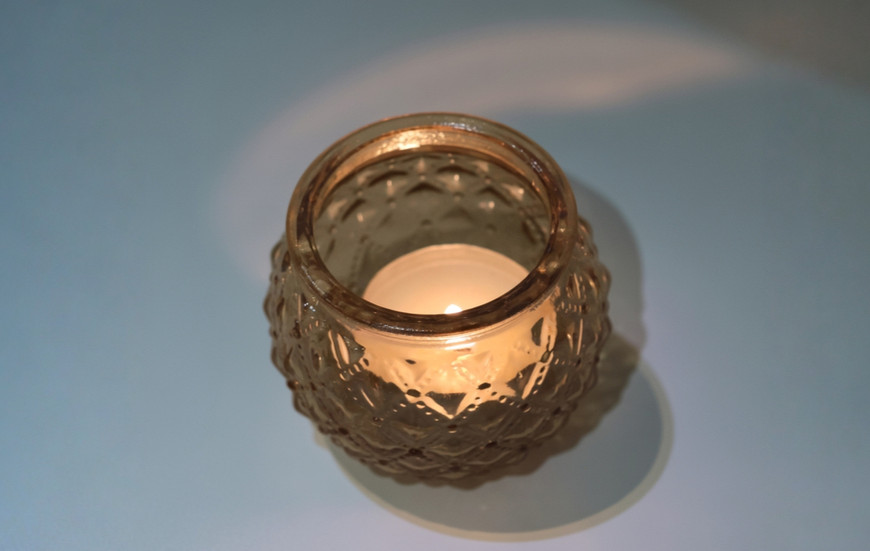 Bee wax tealight candle glowing warmly inside a holder, cosy atmosphere.