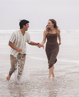 Romantic candid engagement photography of a couple running barefoot through ocean waves at Manhattan Beach, California, featuring natural light, coastal scenery, and intimate couple moments.