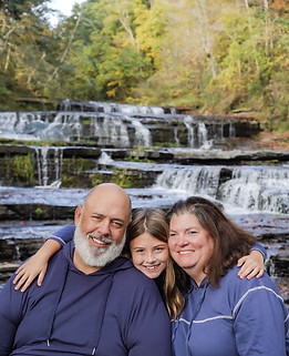 Happy family posing together in matching outfits during a scenic family photoshoot at Sun Valley Campsites with a beautiful waterfall in the background.