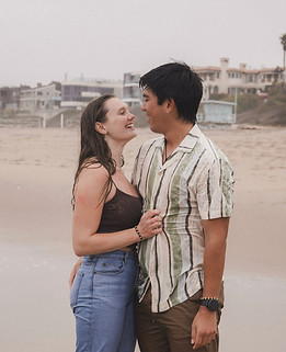 A romantic and candid beachside moment of a couple with wet hair and casual outfits, embracing and smiling, beautifully capturing the intimacy and joy of their engagement photoshoot at Manhattan Beach, California.