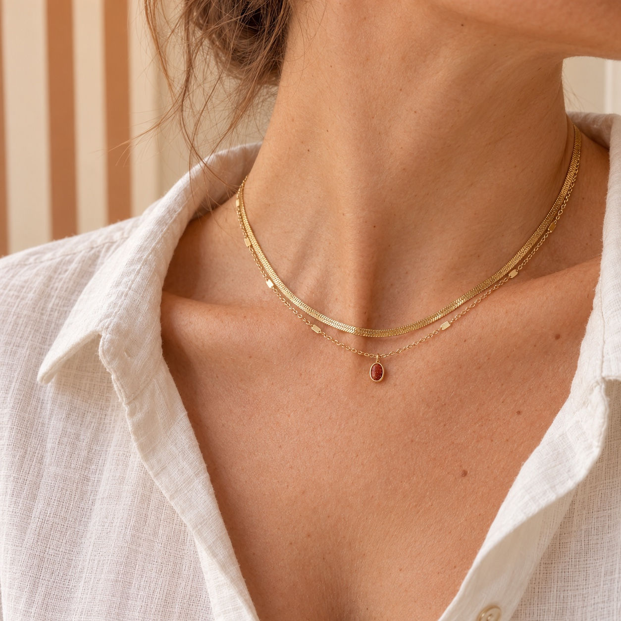 Collier sable d’or BOHM PARIS doré porté, avec deux chaînes et petit pendentif ovale brun scintillant.