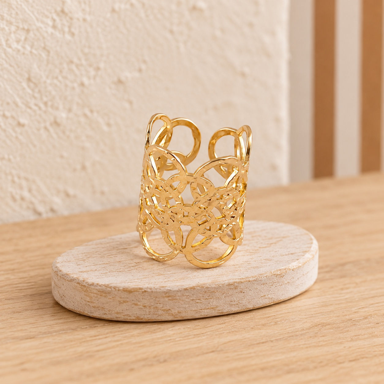 Bague large cercles ajourés BOHM PARIS dorée, présentée sur un socle beige dans un décor aux tons naturels.