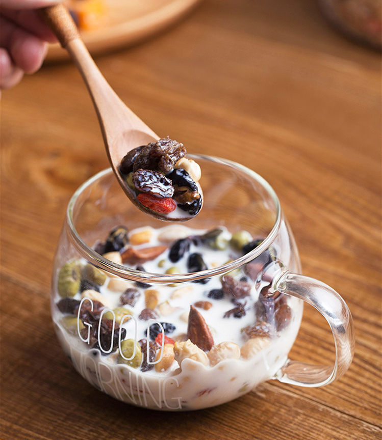 Wooden spoon lifting dried fruit from a glass bowl of milk and nuts.