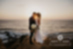 Bride and groom standing on a cliff over the ocean at sunset