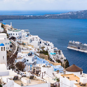 Coastal view of Santorini with white buildings, blue-domed churches, and a cruise ship on the Aegean Sea, conveying a serene, picturesque scene.